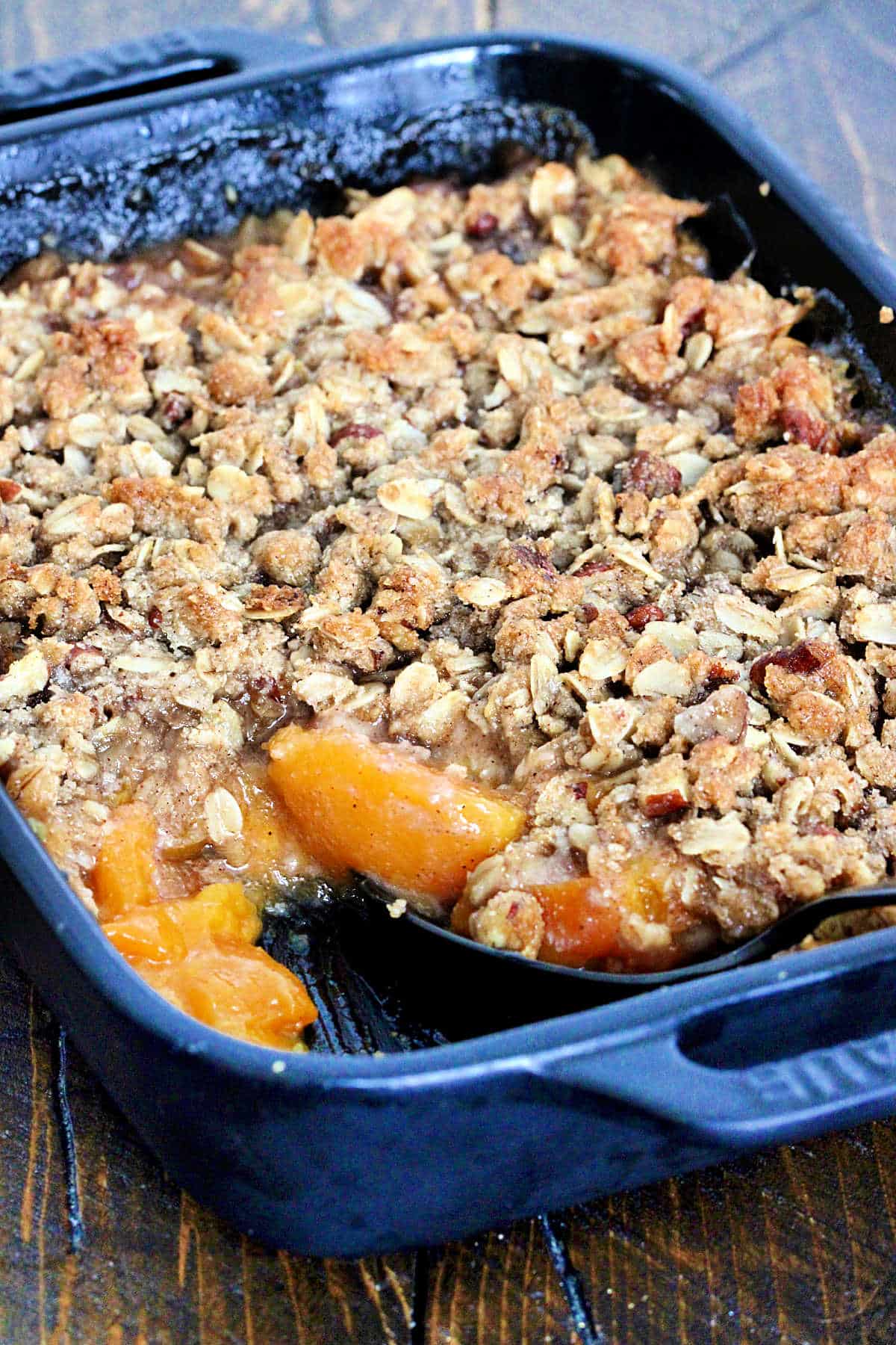 Gluten free peach crisp in a black baking dish with a scoop taken out.
